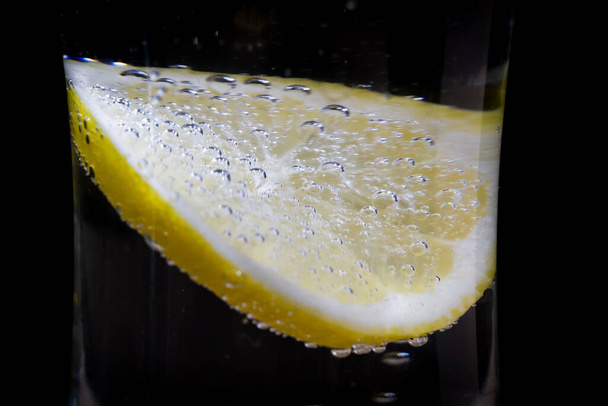 ένα ποτήρι φρέσκο πόσιμο νερό και λεμόνι σε μαύρο φόντο. φυσαλίδες σε ένα γυάλινο μεταλλικό νερό ως αποσβεστήρας δίψας. - Φωτογραφία, εικόνα