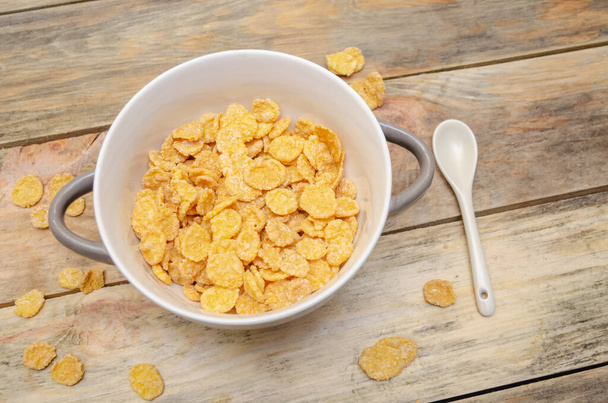 Bowl of cornflakes with a white spoon on a wooden background - Foto, Imagen