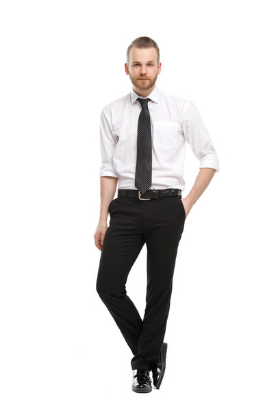 A young man with a beard in an everyday shirt stands tall and holds one hand in his trouser pockets, isolated on a white background. - Foto, immagini