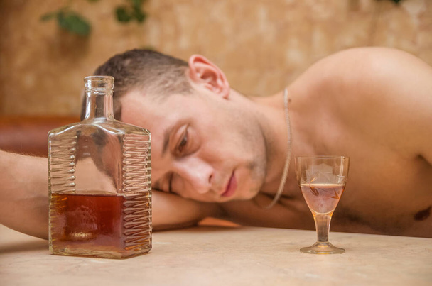 Alkoholisti. Pöydässä oleva mies nukkuu alkoholipullon ja lasin lähellä. Vaarallinen tapa. Epäterveellisen elämän käsite. Sosiaalinen ongelma. - Valokuva, kuva