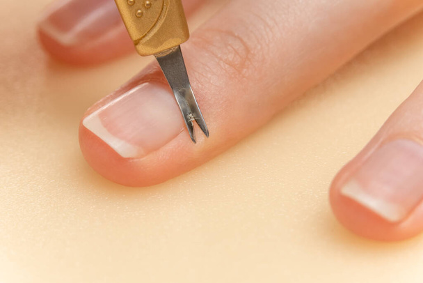 Meisje doet haar eigen manicure. Nagelriemen verwijderen van de vinger met behulp van een speciaal gereedschap close-up - Foto, afbeelding