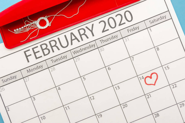 Calendar with a painted heart on February 14, red box with a silver chain with a pendant on a blue background. Concept of Valentine's day, holiday - Photo, Image