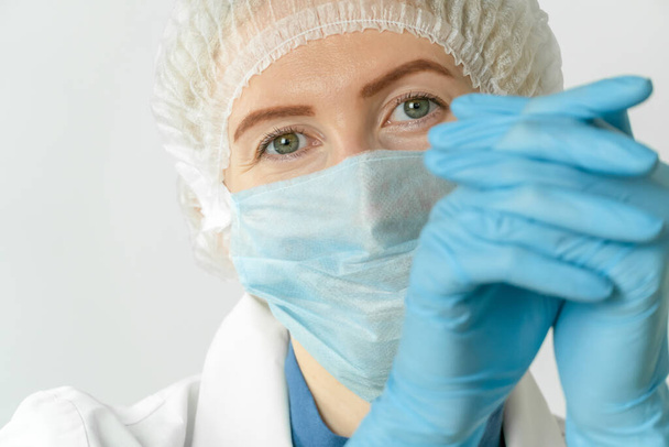 Retrato de una hermosa joven doctora con un vestido médico, máscara médica y gorra con la cabeza apoyada en la mano. Médico cansado - Foto, Imagen
