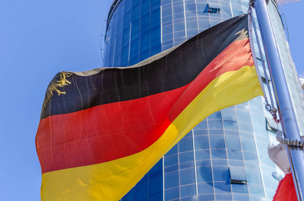 German flag on the background of a modern glass building and blue sky close-up - Photo, Image