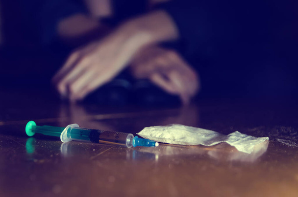 jeringa y drogas con un hombre desenfocado sentado en el suelo y sus manos. concepto de adicción. Foto teñida - Foto, Imagen