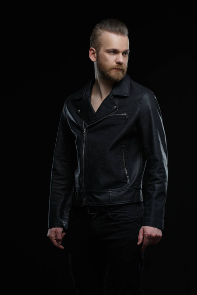 Cute bearded man in a black leather jacket isolated on a black background. - Photo, Image