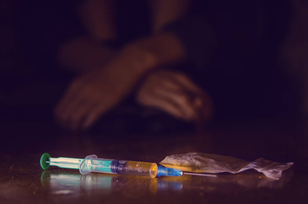 jeringa y drogas con un hombre desenfocado sentado en el suelo y sus manos. concepto de adicción - Foto, Imagen
