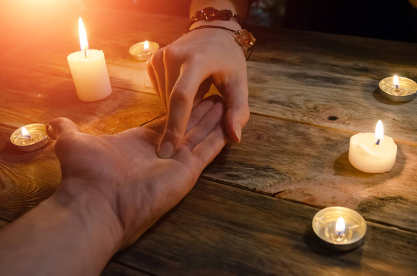 Женщина-гадалка читает линии руки мужчины и предсказывает его будущее, руки на деревянном фоне среди свечей. концепция магии, гадание - Фото, изображение