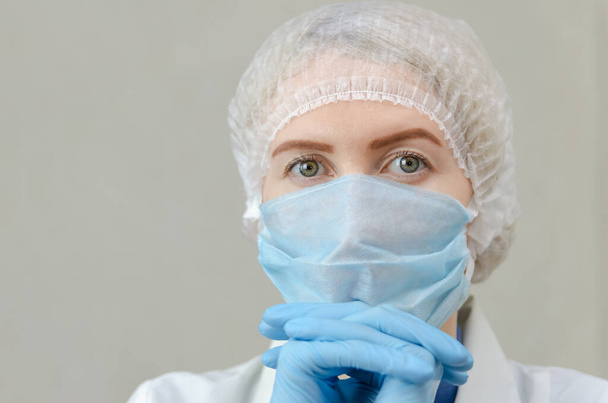Egy gyönyörű doktornő portréja orvosi köpenyben, orvosi maszkkal és sapkával a kezén. Fáradt orvos - Fotó, kép
