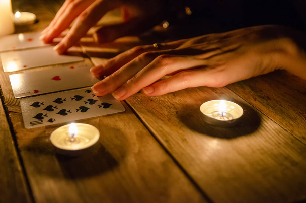Mains d'une diseuse de bonne aventure et cartes sur la table, autour de bougies allumées dans l'obscurité sur une table en bois. concept de divination, magie - Photo, image