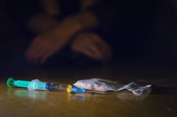 injectiespuit en drugs met een gedeconcentreerde man op de vloer en zijn handen. Het begrip verslaving - Foto, afbeelding