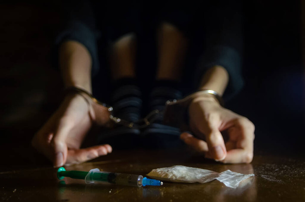 strzykawka i narkotyki z nieskupionym mężczyzną siedzącym na podłodze i zamkniętymi rękami w kajdankach.Narkoman. - Zdjęcie, obraz