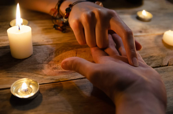 donna indovino legge le linee della mano di un uomo e predice il suo futuro, le mani su uno sfondo di legno tra le candele. concetto di magia, divinazione - Foto, immagini