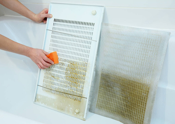 Mulher limpeza filtro de capuz de cozinha na banheira com esponja - Foto, Imagem