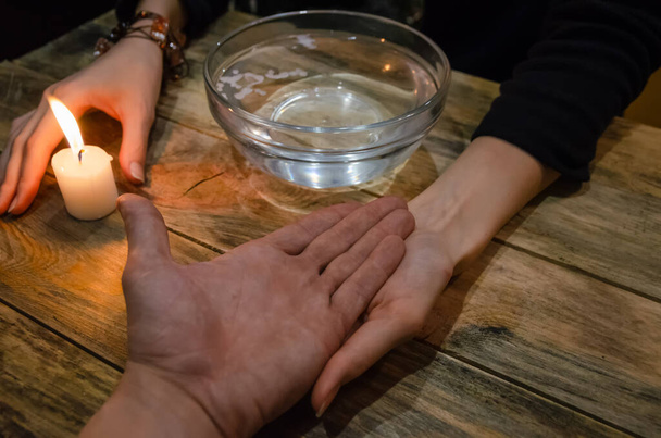 Adivinación con una vela en el agua. la mano de un adivino y la mano de un hombre. concepto de magia, adivinación - Foto, Imagen