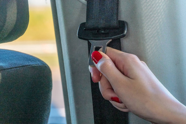 La mano femenina toma un cinturón de seguridad para abrocharse el cinturón antes de montar. Primer plano de una mano femenina con cinturón de seguridad - Foto, imagen