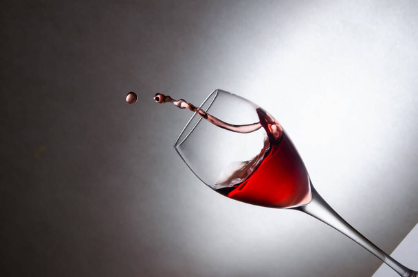 Glass with splashes, drops of red wine on a white background. Freezing liquids in motion. Glass of red wine at an angle with copy space - Photo, Image