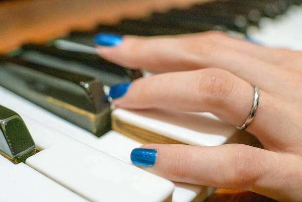 Nahaufnahme der Hände einer jungen Frau mit blauem Nagellack beim Klavierspielen - Foto, Bild