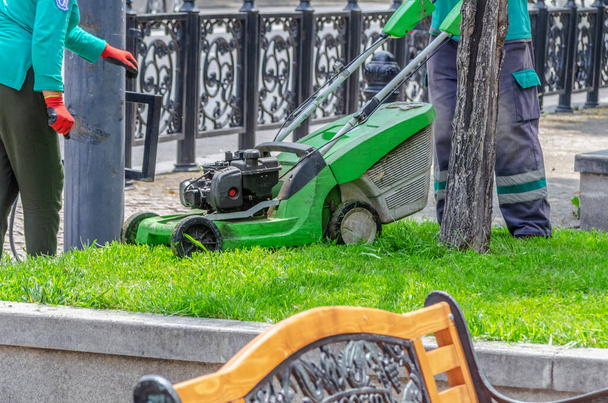 Близько - до робітників з газонокосаркою косячи зелену траву на вулицях в сонячний день
 - Фото, зображення