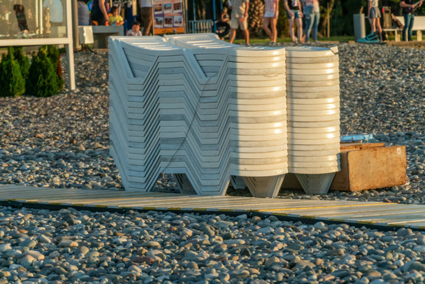 Sunbeds collected in a pile after sunset on the sea with a pebble beach; Batumi - Photo, Image