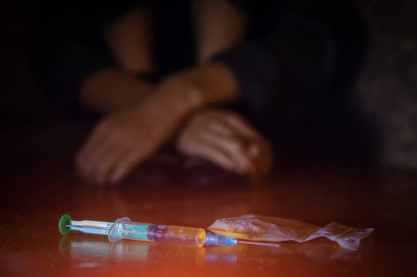 Spritze und Drogen mit einem defokussierten Mann auf dem Boden sitzend und seine Hände. Begriff der Sucht - Foto, Bild