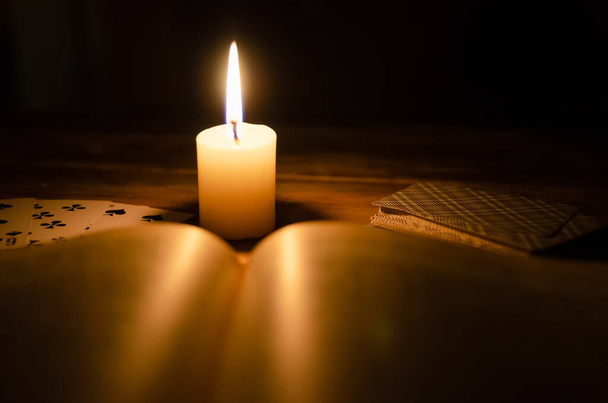 Мистическая атмосфера, карты, книга, зажженная свеча в темноте на деревянном столе. Эзотерика, гадание и прочее - Фото, изображение