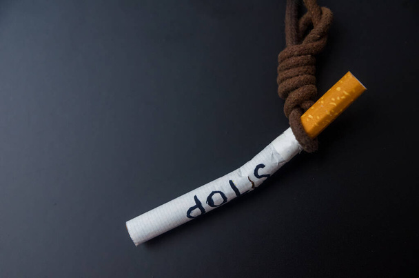Opknoping sigaret op zwarte achtergrond. Pleeg zelfmoord. Stoppen met roken concept. wereld geen tabak dag - Foto, afbeelding