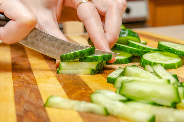 Female hand cuts cucumbers with a knife on the bars on a wooden plank close up - Valokuva, kuva