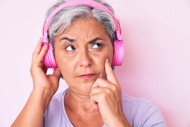 ヘッドフォンを使用して音楽を聴くシニアパニック女性深刻な顔あごに手で質問について考える,混乱のアイデアについて思慮深い  - 写真・画像