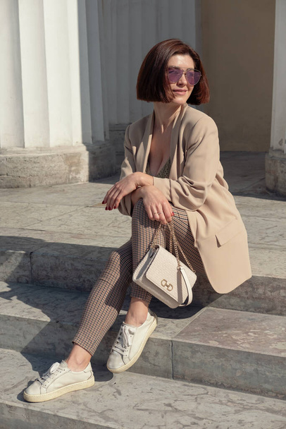 Outdoor fashion portrait of a  young womasitting on the steps of a building. Photo of beautiful stylish brunette woman in the city. Fashion fall autumn spring photo - Fotografie, Obrázek