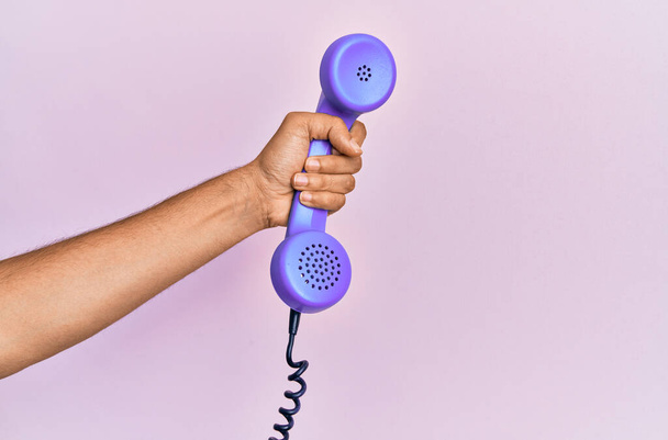 Hispanic hand holding vintage telephone over isolated pink background. - Foto, Imagen