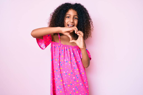 African american child with curly hair wearing casual dress smiling in love doing heart symbol shape with hands. romantic concept.  - Fotoğraf, Görsel