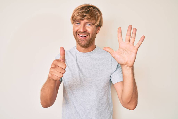 Молодий блондинка в повсякденному одязі показує і вказує пальцями номер шість, посміхаючись впевнено і щасливо
.  - Фото, зображення