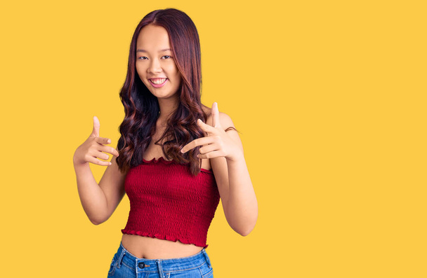 Young beautiful chinese girl wearing casual clothes pointing fingers to camera with happy and funny face. good energy and vibes.  - Zdjęcie, obraz