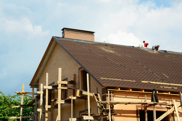 Scena di costruzione di tetti sfocati con costruttori edili su un tetto di una grande casa in mattoni con impalcature. - Foto, immagini