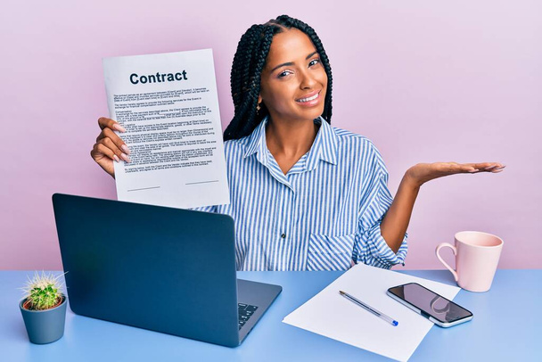 Beautiful hispanic woman at the office showing contract document celebrating achievement with happy smile and winner expression with raised hand  - Foto, afbeelding