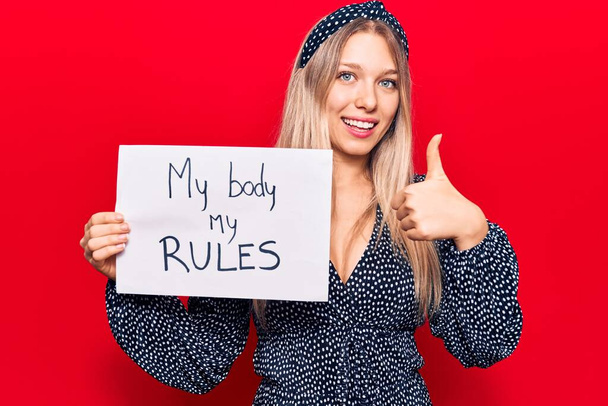 Young blonde woman holding my body my rules banner smiling happy and positive, thumb up doing excellent and approval sign  - Фото, зображення