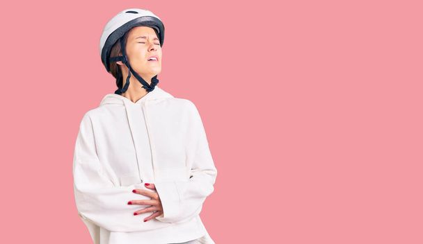 Schöne brünette junge Frau mit Fahrradhelm und sportlicher Kleidung mit der Hand auf dem Bauch, weil Übelkeit, schmerzhafte Krankheit fühlen sich unwohl. Schmerzkonzept.  - Foto, Bild