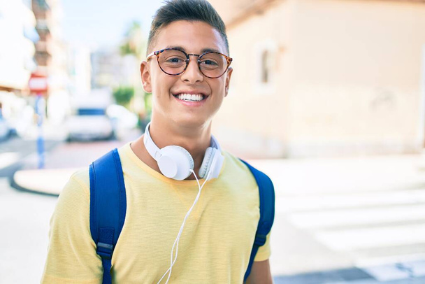 Mladý hispánský student usměvavý šťastný pomocí sluchátek chůze na ulici města - Fotografie, Obrázek