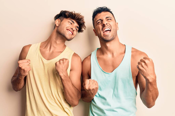 Νεαρό γκέι ζευγάρι φορώντας casual ρούχα ενθουσιασμένοι για την επιτυχία με τα χέρια ψηλά και τα μάτια κλειστά γιορτάζει τη νίκη χαμογελώντας. έννοια νικητή.  - Φωτογραφία, εικόνα