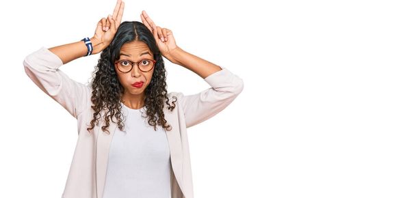 Jeune fille afro-américaine portant des vêtements de travail faisant geste d'oreilles de lapin avec les mains paumes regardant cynique et sceptique. concept lapin de Pâques.  - Photo, image