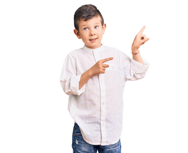 Cute blond kid wearing elegant shirt pointing aside worried and nervous with both hands, concerned and surprised expression  - 写真・画像