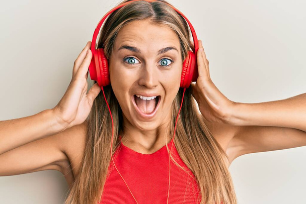 Young blonde woman listening to music using headphones celebrating crazy and amazed for success with open eyes screaming excited.  - Foto, Imagem