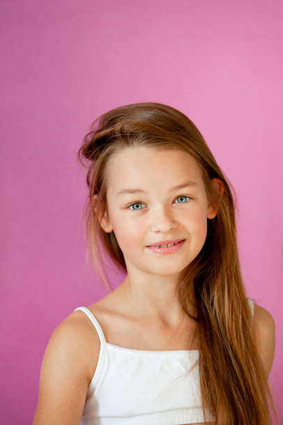 πορτρέτο ενός ήπιου εννιάχρονου κοριτσιού με μακριά μαλλιά σε έναν λιλά τοίχο. - Φωτογραφία, εικόνα