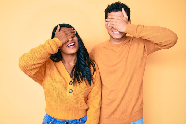 Beautiful latin young couple wearing casual clothes together smiling and laughing with hand on face covering eyes for surprise. blind concept.  - Photo, Image