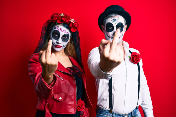 Couple wearing day of the dead costume over red showing middle finger, impolite and rude fuck off expression  - Photo, Image