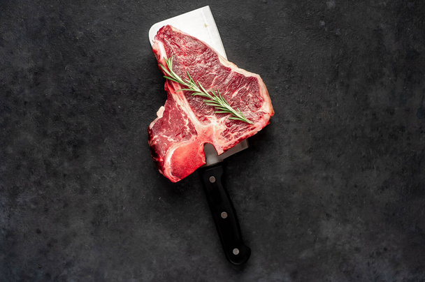 vista de cerca del filete crudo de hueso t con ingredientes en un cuchillo de carne sobre fondo de piedra - Foto, Imagen