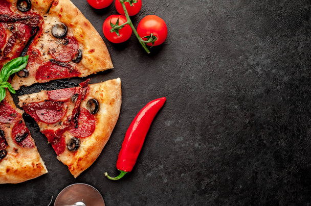 délicieuse pizza pepperoni tranchée avec saucisses au salami, mozzarella, olives, herbes provençales sur fond de pierre - Photo, image