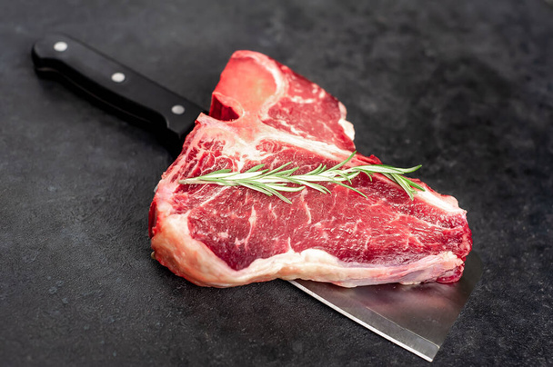 closeup view of raw t-bone steak with ingredients on a meat knife  on stone background - Foto, Imagen