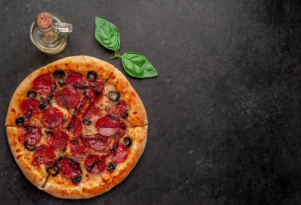 pizza pepperoni com salsichas de salame, mussarela, azeitonas, ervas provençais em um fundo de pedra - Foto, Imagem